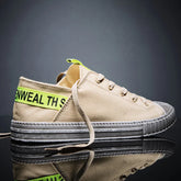 Beige canvas low-top sneaker with neon yellow accent and thick grey rubber sole, streetwear style