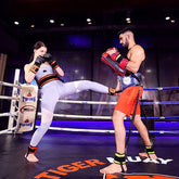 Woman in light grey fitted athletic leggings and matching top practicing kickboxing in a ring
