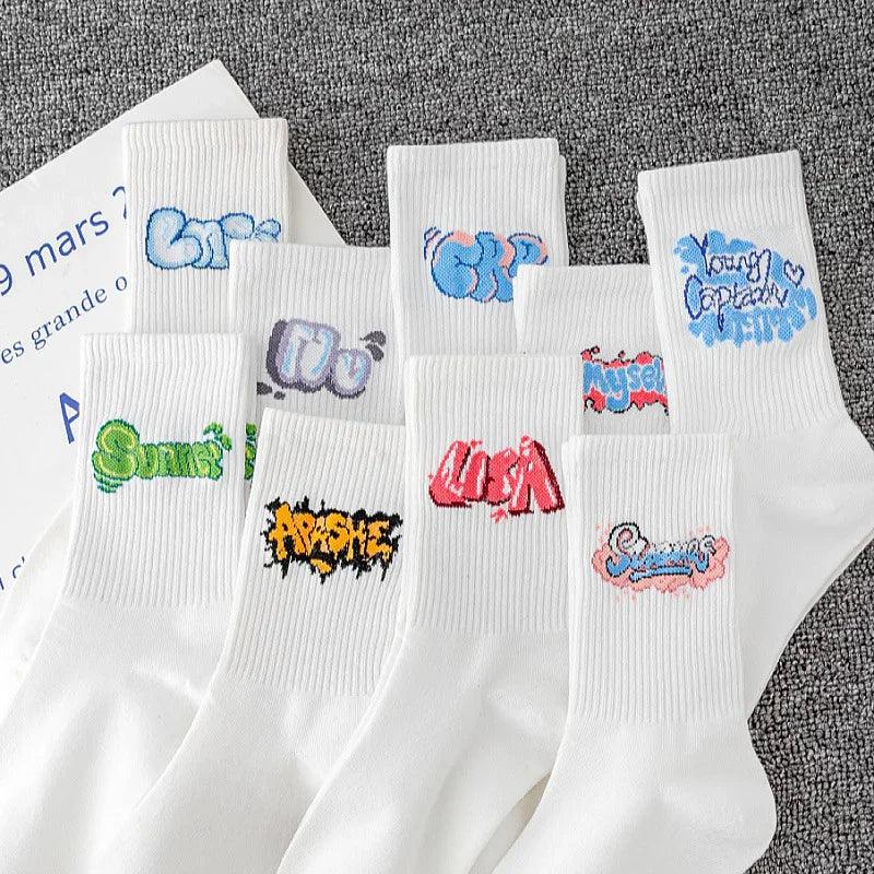 White cotton crew socks with colorful graffiti-style text embroidery, laid out on grey fabric