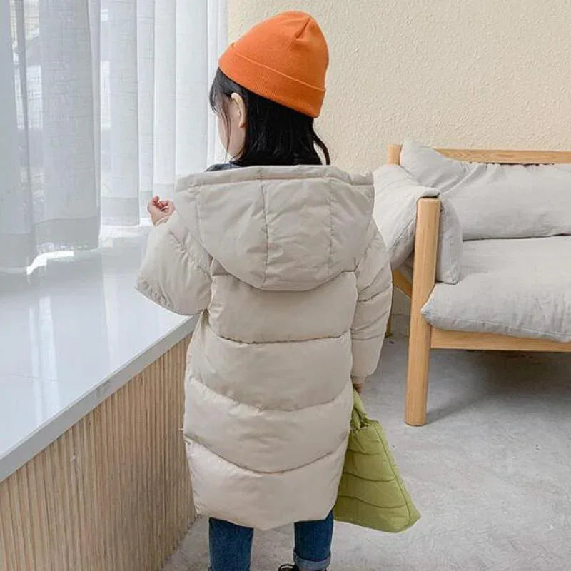 Child wearing long beige puffer coat with hood, orange beanie, and casual jeans indoors