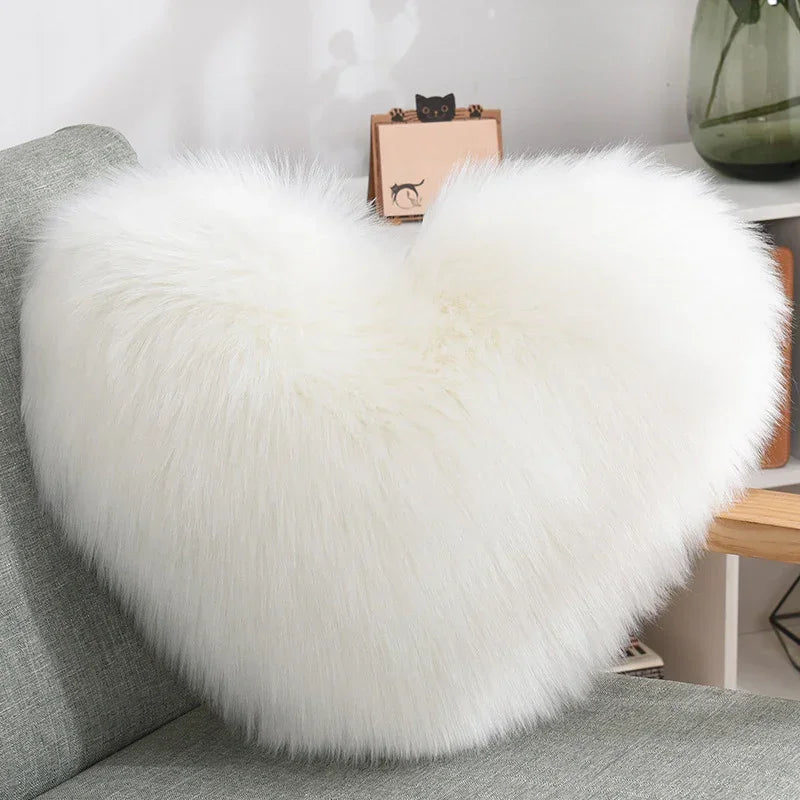 White fluffy heart-shaped faux fur pillow on a modern grey sofa