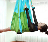Woman in black mesh long sleeve bodysuit using green and blue aerial yoga hammock indoors