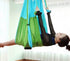 Woman in black mesh long sleeve bodysuit using green and blue aerial yoga hammock indoors