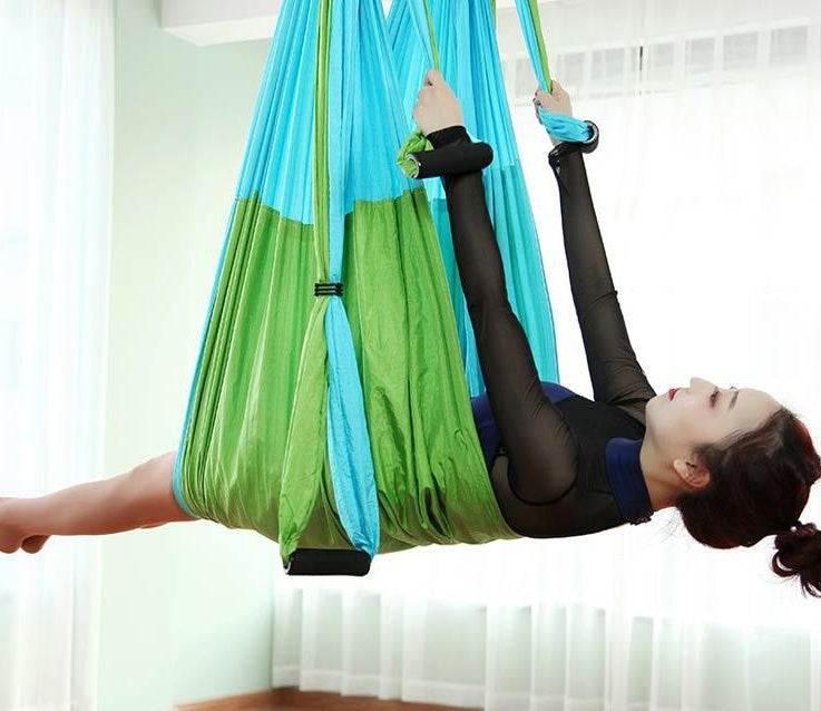 Woman in black mesh long sleeve bodysuit using green and blue aerial yoga hammock indoors