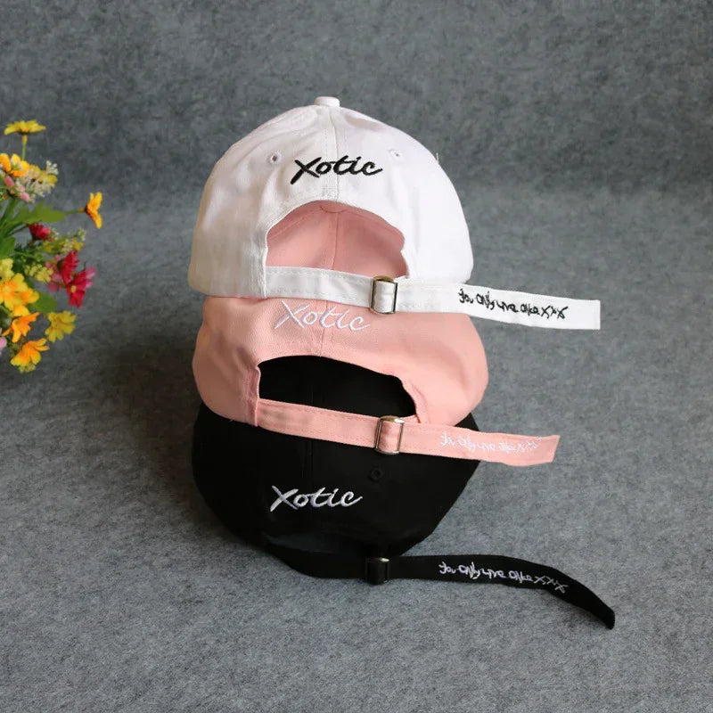 Stack of three embroidered cotton baseball caps in white, pink, and black with adjustable straps