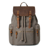 Gray canvas backpack with brown leather flap, buckle straps, and zip pockets, casual fit.
