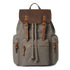 Gray canvas backpack with brown leather flap, buckle straps, and zip pockets, casual fit.