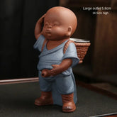 Ceramic figurine of a child monk in blue robe with basket and boots, 16.5cm high.