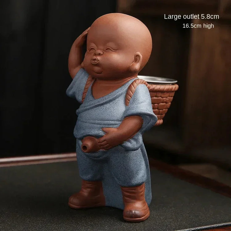 Ceramic figurine of a child monk in blue robe with basket and boots, 16.5cm high.