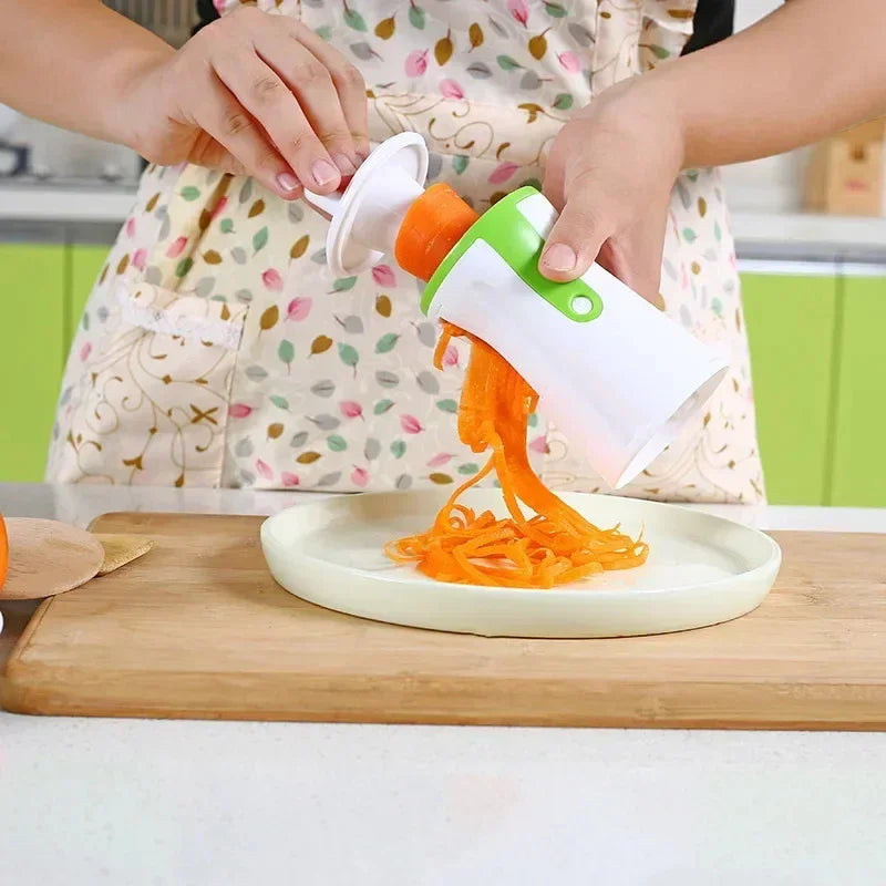 Person wearing a colorful apron with leaf print, using a white and green spiralizer kitchen tool to make carrot noodles, apron fits loose and casual.