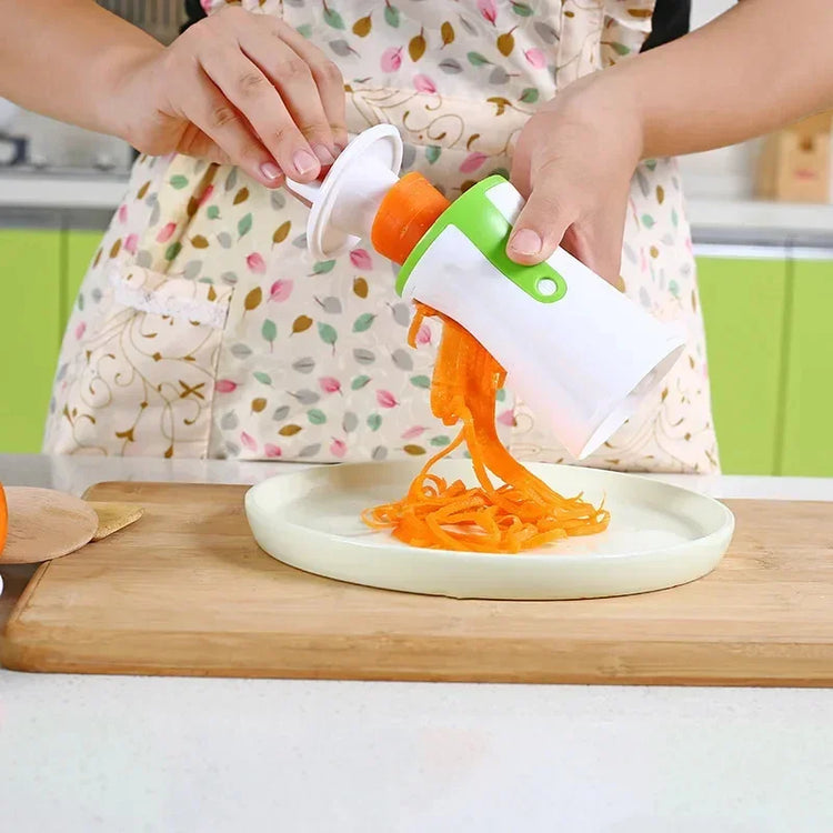 Person wearing a colorful apron with leaf print, using a white and green spiralizer kitchen tool to make carrot noodles, apron fits loose and casual.
