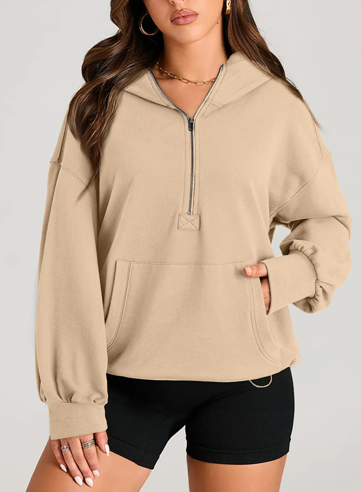 Woman wearing a beige oversized quarter-zip hoodie with kangaroo pocket and black fitted shorts