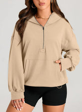Woman wearing a beige oversized quarter-zip hoodie with kangaroo pocket and black fitted shorts