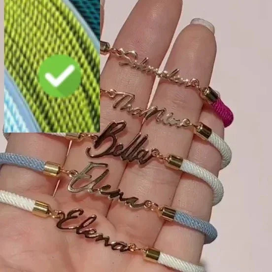Hand holding personalized name bracelets with gold-tone metal and colorful cord, modern style.