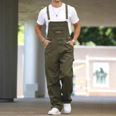 Man wearing loose olive green denim overalls and a white t-shirt, casual streetwear style.