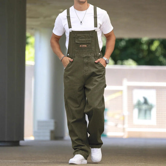 Man wearing loose olive green denim overalls and a white t-shirt, casual streetwear style.