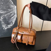Brown faux leather shoulder bag with front pockets, structured shape, and long handles