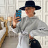 Woman in a light gray oversized hoodie and joggers, wearing a black wide-brim hat, taking a mirror selfie.