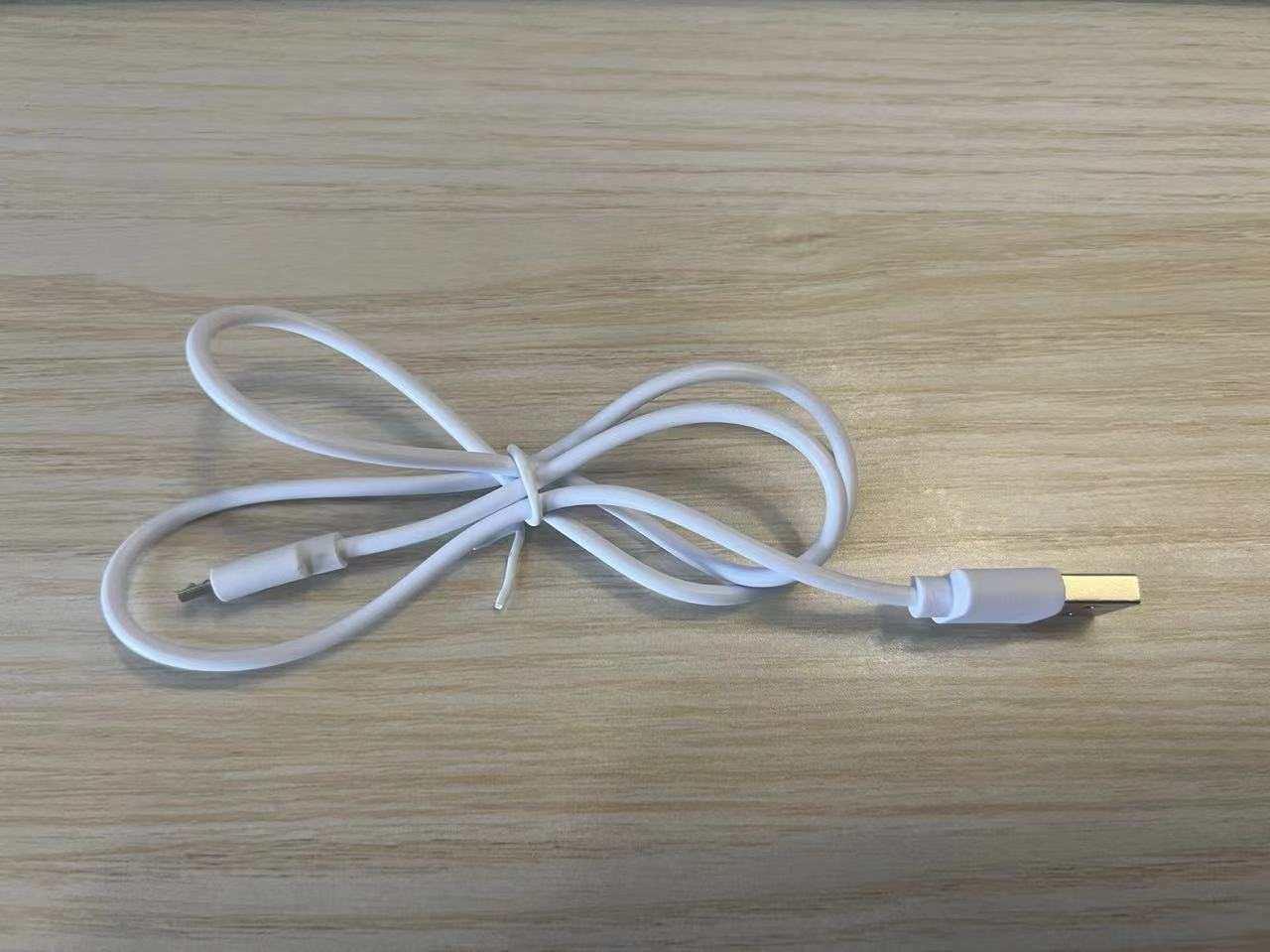White USB charging cable with micro USB connector, flexible plastic material, on wood surface