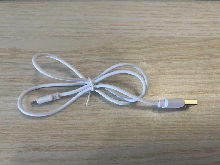 White USB charging cable with micro USB connector, flexible plastic material, on wood surface