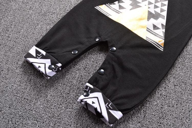 Black baby romper with geometric print, snap buttons, and patterned cuffs on gray carpet