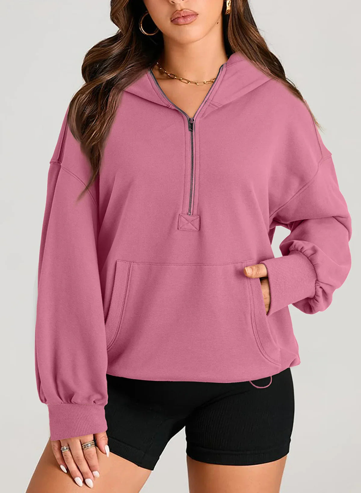 Woman wearing a loose fit pink pullover hoodie with half-zip front and kangaroo pocket, paired with black shorts