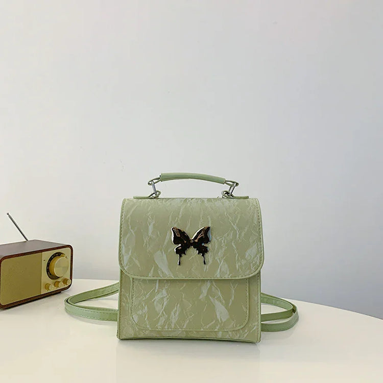 Light green faux leather crossbody bag with butterfly embellishment and top handle