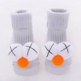 Gray ribbed knit baby socks with soft plush white and orange pompom accents on toes