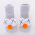 Gray ribbed knit baby socks with soft plush white and orange pompom accents on toes