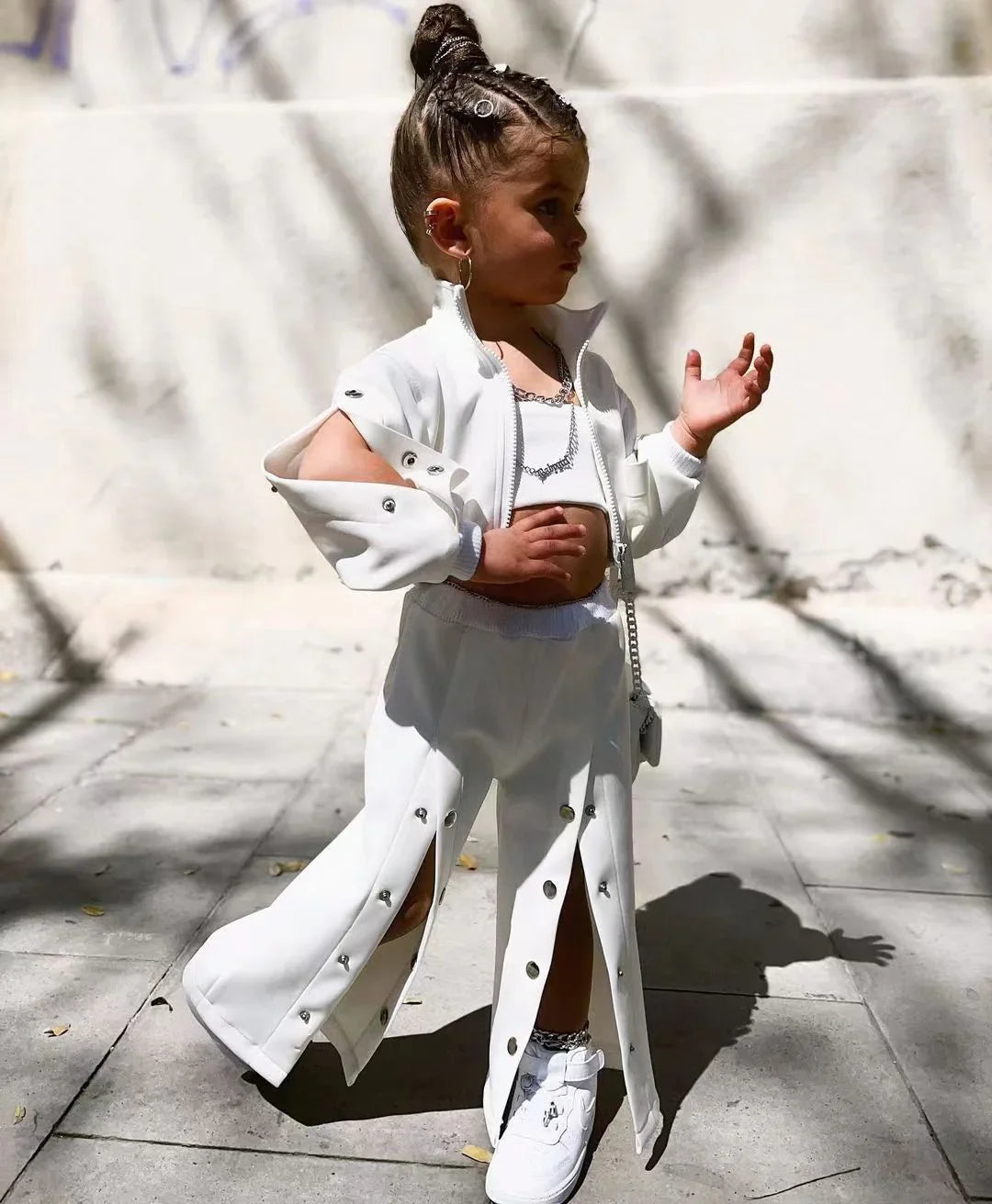 Child wearing white streetwear set with snap buttons, wide-leg pants, crop top, and sneakers