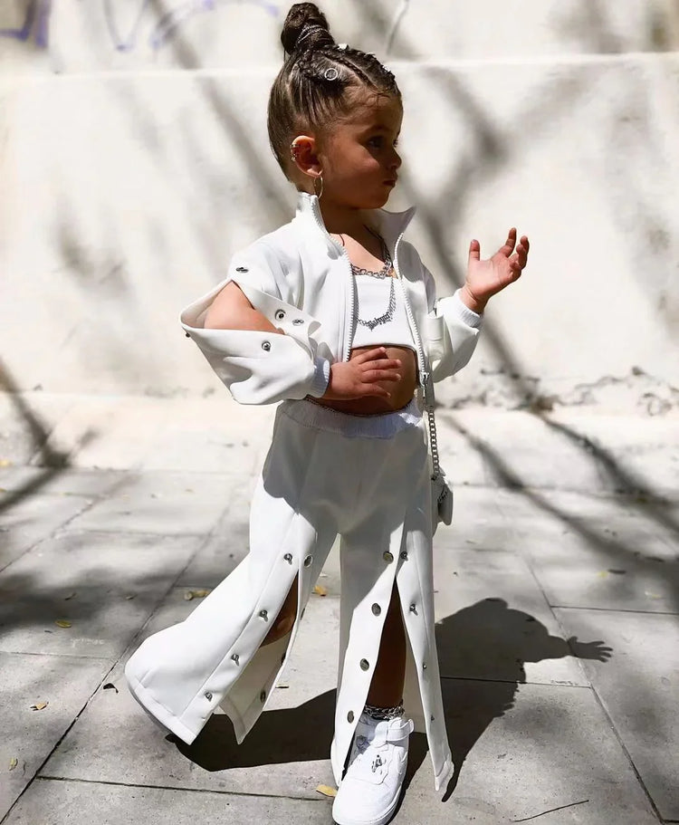 Child wearing white streetwear set with snap buttons, wide-leg pants, crop top, and sneakers