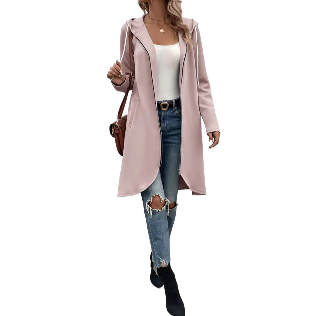 Woman wearing a light pink hooded longline coat, white tank top, ripped blue jeans, black ankle boots