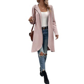 Woman wearing a light pink hooded longline coat, white tank top, ripped blue jeans, black ankle boots