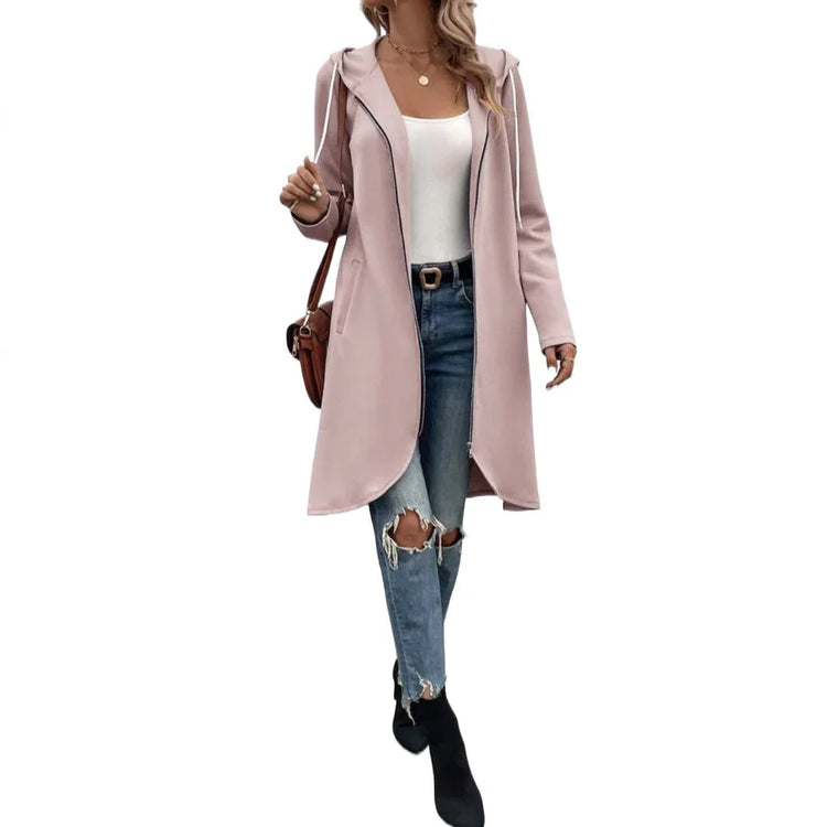 Woman wearing a light pink hooded longline coat, white tank top, ripped blue jeans, black ankle boots
