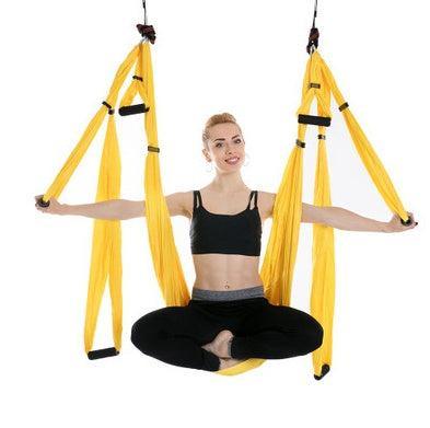 Woman in black sportswear using bright yellow aerial yoga swing, sporty fit style