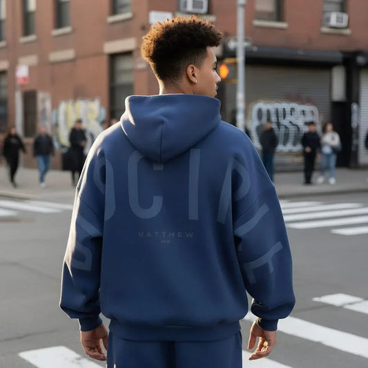 Man wearing oversized blue streetwear hoodie with graphic back print on city street