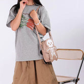 Woman in oversized grey carrot graphic t-shirt and tan skirt, holding tan skeleton crossbody bag