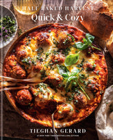 Cover of Half Baked Harvest Quick & Cozy cookbook by Tieghan Gerard featuring a baked cheesy meatball dish with fresh herbs and bread on wooden table