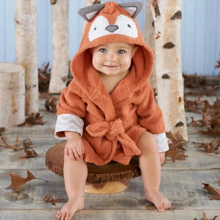 Baby in orange hooded terry robe with fox ears and face, sitting in woodland setting