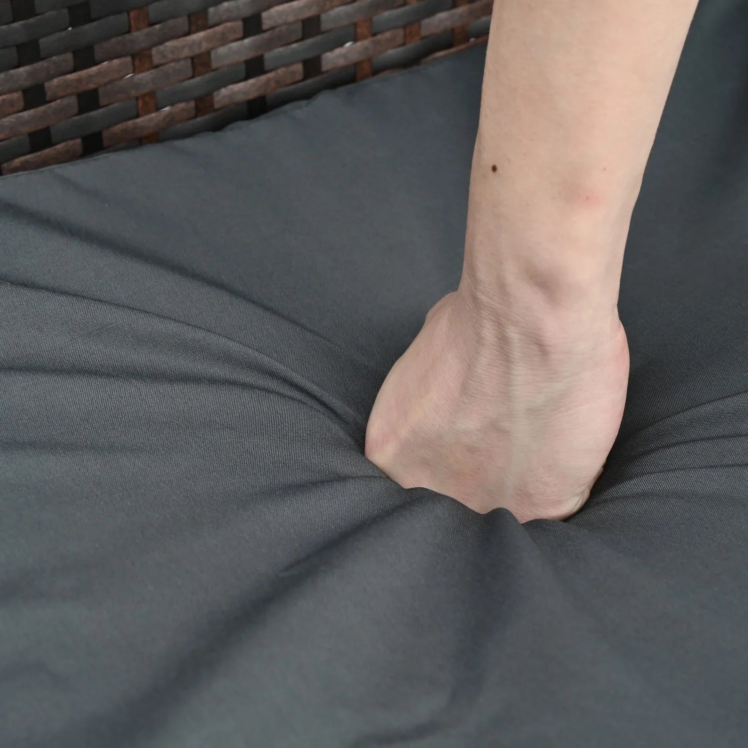 Hand pressing into soft, dark gray fabric cushion to show plush, durable material