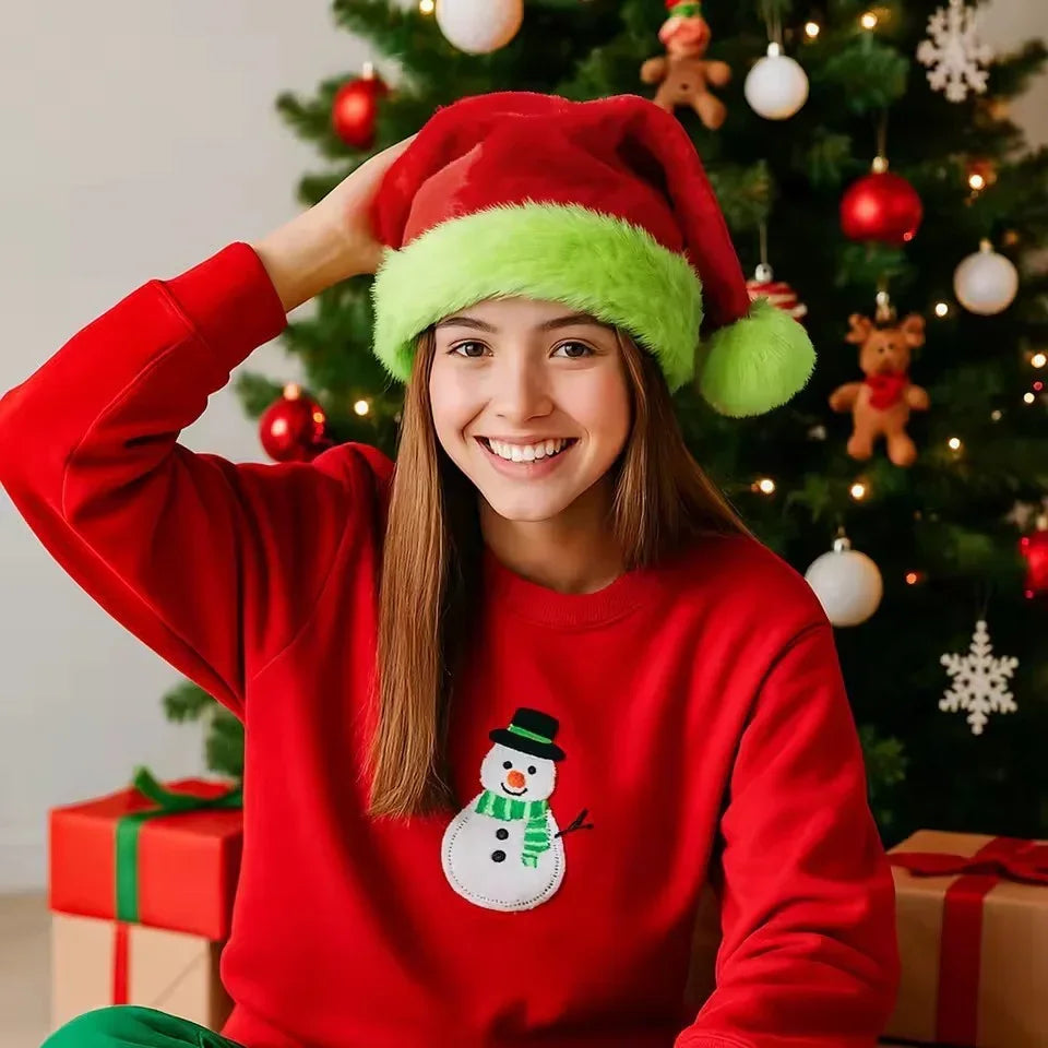 Woman wearing red Christmas sweater with snowman design and red Santa hat with green trim, sitting by decorated tree.