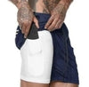 Navy blue athletic shorts with white compression liner, stretch fabric, relaxed fit, tattooed model