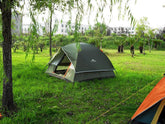 Green waterproof camping tent with mesh windows set up on grassy outdoor field