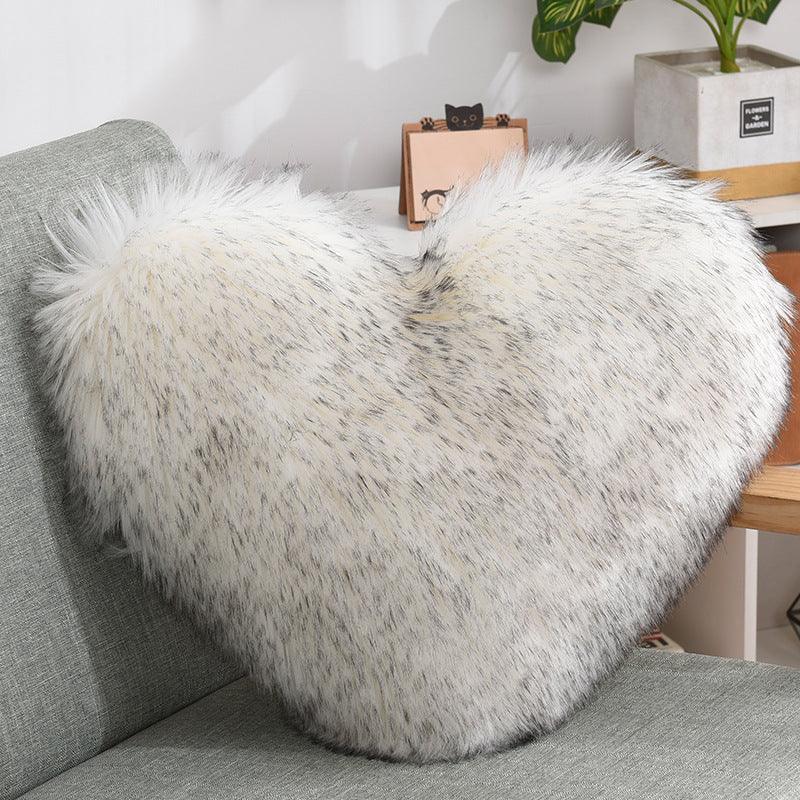 White faux fur heart-shaped pillow with grey specks on a gray sofa, cozy decor accent