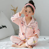 Child in light pink cartoon strawberry print pajamas with black trim, relaxed fit, sitting on bed