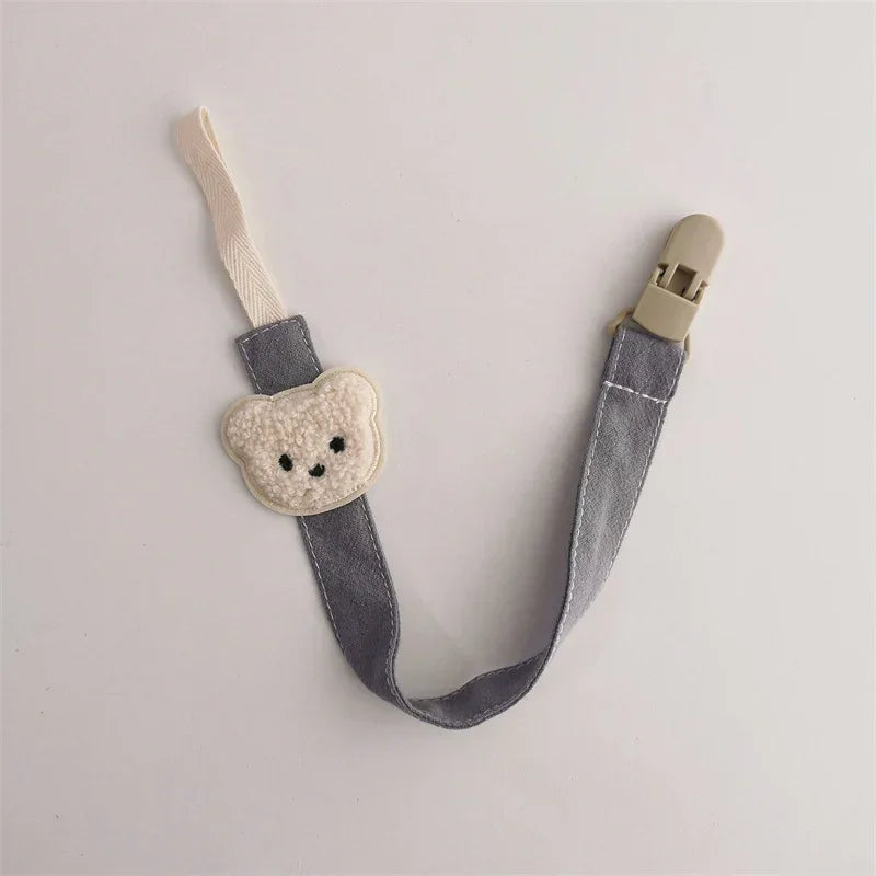 Gray fabric pacifier clip with cream bear motif, metal clasp, and woven strap.