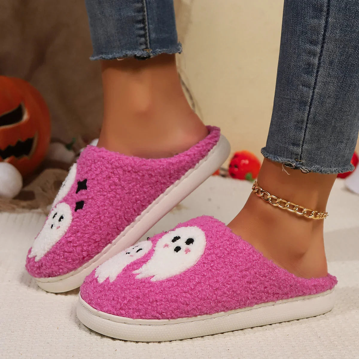 Pink fuzzy slip-on slippers with white ghost pattern, worn with frayed hem jeans