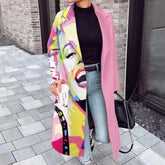 Woman wearing a long pink colorblock streetwear coat with bold abstract face print, paired with jeans