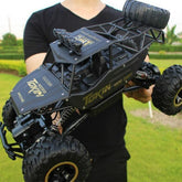 Person in a fitted black t-shirt holding a matte black oversized RC off-road car outdoors.