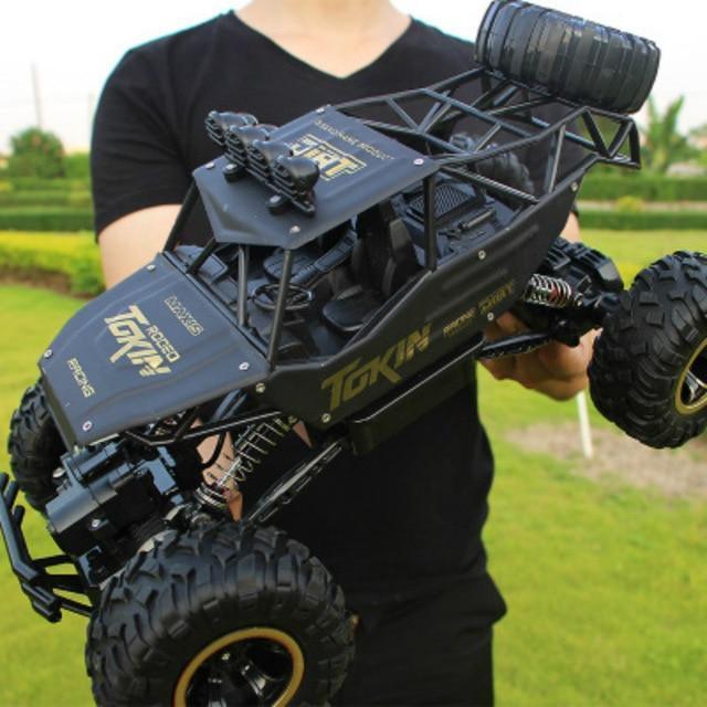 Person in a fitted black t-shirt holding a matte black oversized RC off-road car outdoors.